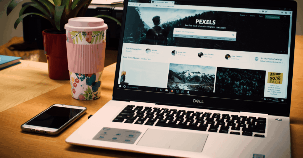 A laptop, cellphone and coffee tumbler on a desk