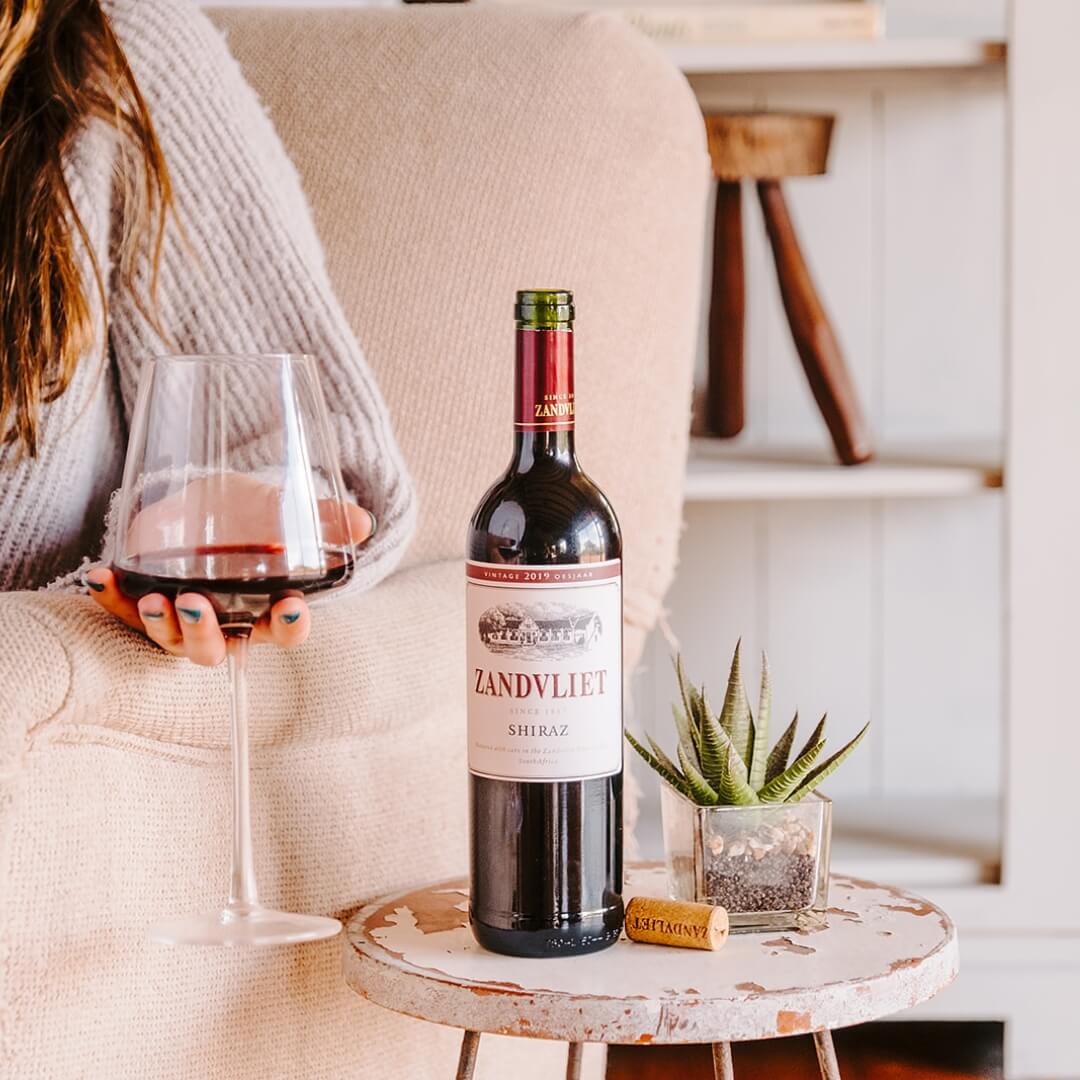 Zandvliet Case Study Image - A lady holding a glass of wine with a bottle of Zandvliet Shiraz on the table next to her